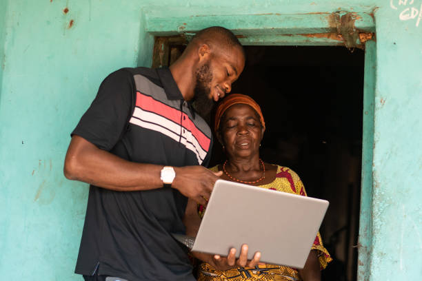 A young African man explaining to an elderly african woman how to use the laptop